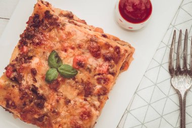 Kıyma, domates sosu ve beyaz plaka üzerinde taze fesleğen ile ev yapımı lazanya