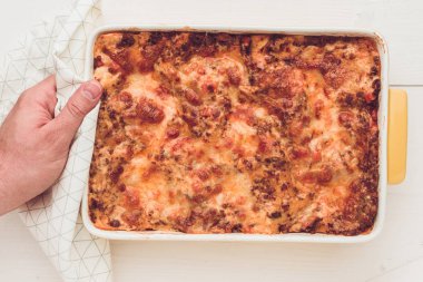 El İtalyan lazanya Bolognese sığır eti, domates sosu ve rustik beyaz ahşap masa üzerinde yeşil fesleğen ile hizmet vermektedir