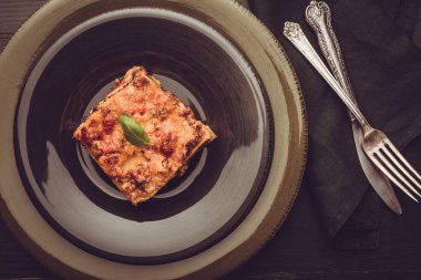 Kıyma, domates sosu ve karanlık plaka üzerinde yeşil fesleğen ile geleneksel İtalyan lazanya