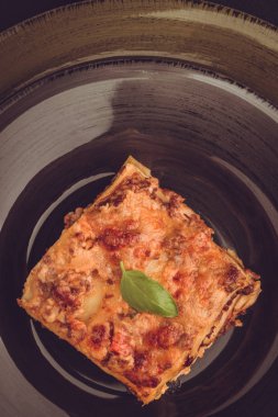 Kıyma, domates sosu ve karanlık plaka üzerinde yeşil fesleğen ile geleneksel İtalyan lazanya