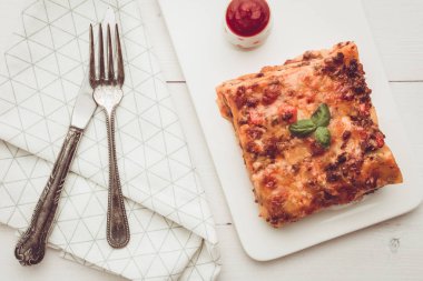 Kıyma, domates sosu ve beyaz plaka üzerinde taze fesleğen ile ev yapımı lazanya