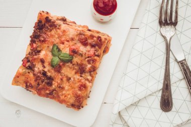 Kıyma, domates sosu ve beyaz plaka üzerinde taze fesleğen ile ev yapımı lazanya