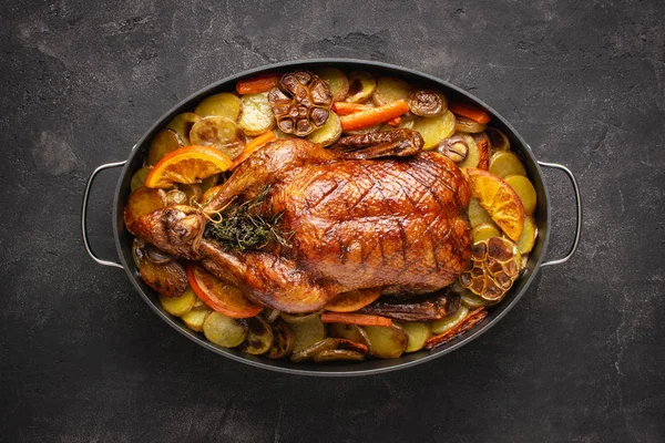 Roasted Whole Duck with Potatoes, Carrots and Oranges on Rustic Dark Stone Background