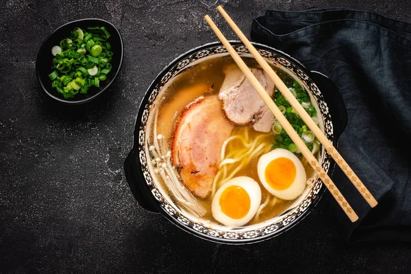 Japanische Ramen-Suppe mit Udonnudeln, Schweinefleisch, Eiern und Schalotten auf dunklem Steingrund — Stockfoto