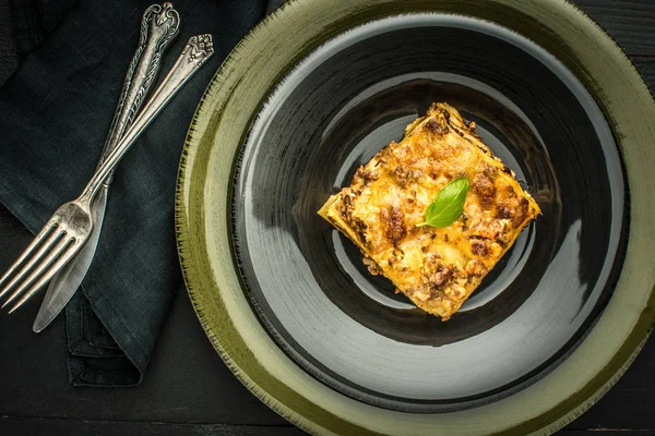 Итальянская лазанья с мясом и зеленым базиликом на темной тарелке — стоковое фото