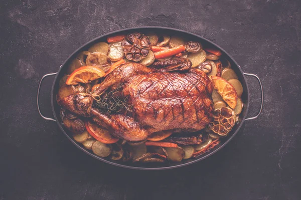 Whole Duck Roasted with Potatoes, Carrots and Oranges on Rustic Dark Stone Background