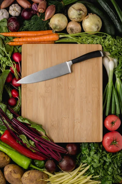 Kitchen Chef Knife on Wood Cutting Board with Fresh Vegetables. Vegan Raw Food. Healthy Eating Concept.