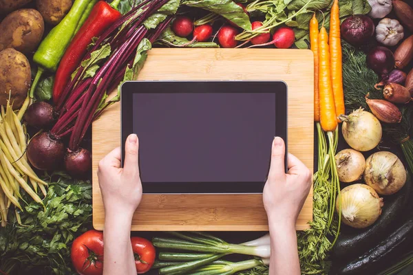 Hands with Tablet over Fresh Organic Vegetables Background. Vegetarian Food Recipes.