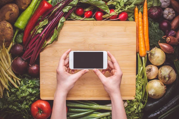 Taze organik sebzeler arka plan üzerinde Smartphone ile hands. Vejetaryen yemek tarifleri.