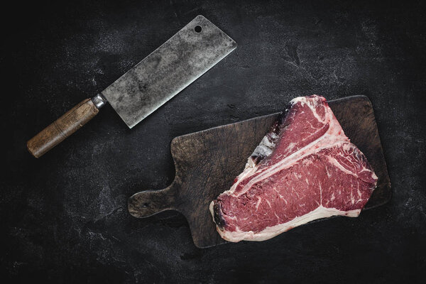 Raw Dry Aged T-bone Steak on Vintage Chopping Board with Meat Cleaver