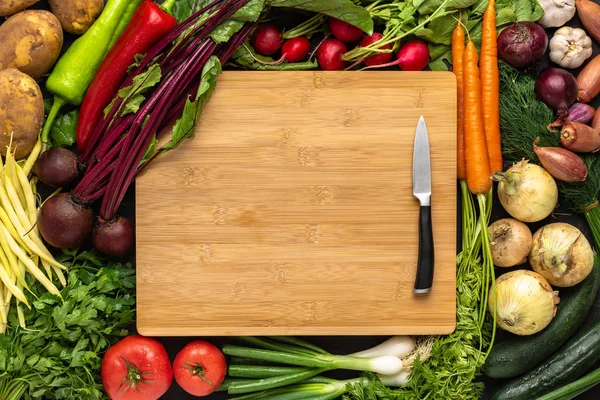 Faca pequena na placa de corte de madeira com fundo de vegetais frescos. Alimentos crus vegetarianos . — Fotografia de Stock
