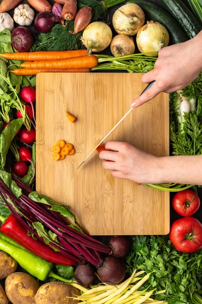 Mãos femininas cortando cenoura orgânica com faca Chef na placa de corte de madeira — Fotografia de Stock