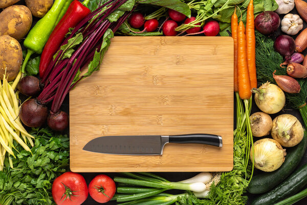 Santoku Knife on Wooden Cutting Board with Fresh Vegetables Background. Vegan Raw Food.