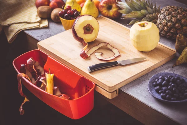 Placa de corte com recipiente de resíduos vermelho com fundo de frutas frescas — Fotografia de Stock