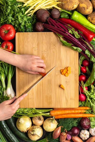 Mãos femininas cortando cenoura orgânica com faca Chef na placa de corte de madeira — Fotografia de Stock