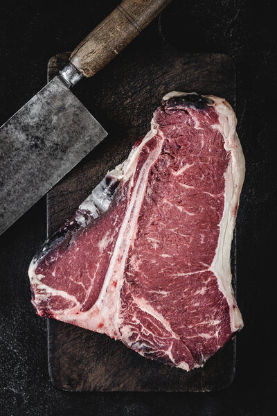 Premium Dry Aged Raw T-bone Steak on Rustic Kitchen Chopping Board