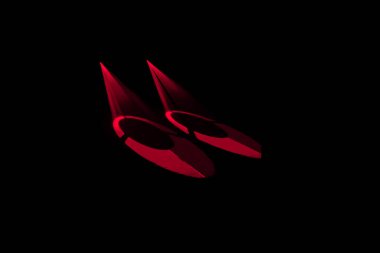 Şık, kırmızı renkli yüksek topuklu ayakkabılar, koyu siyah bir arka plana çarpıcı bir şekilde aydınlatılmış, cazibe ve karmaşıklık hissi uyandırıyor..