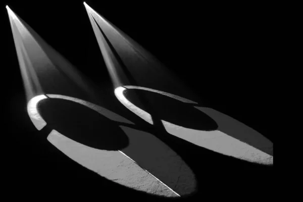 Oval merkezleri olan iki soyut, sivri şekilli sahne ışıkları, siyah arka planda fütüristik ve gizemli bir atmosfer yaratıyor..