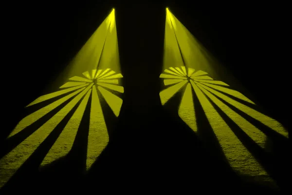 Açılmış yelpazelere benzeyen soyut sarı ışık desenleri kara bir sahneye yansıtılarak dramatik ve sanatsal bir görsel etki yaratıyor..