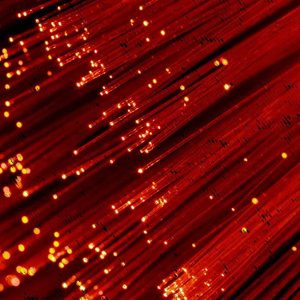 Pek çok ince kırmızı fiber optik tellerin etraflarına yayılmış küçük parlak ışık noktaları, parlak ve soyut desenler oluşturur..