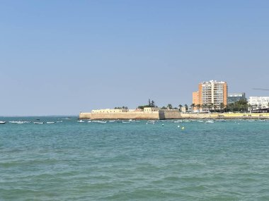 İspanya: Cdiz yakınlarındaki canlı Atlantik kıyı şeridi altın kumlar, tarihi kaleler, çarpan dalgalar ve yaz güneşi altında berrak mavi sular.