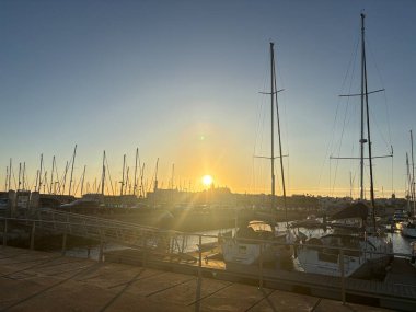 Gün batımında Serene Rota limanı, balıkçı tekneleri, marina rıhtımı ve Cdiz Körfezi üzerinde parlayan turuncu gökyüzüne karşı donanma siluetleri. İspanya