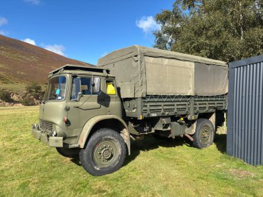 Klasik zeytin sıkıcı kamuflaj, sağlam şasi ve otantik askeri teçhizat içeren, İngiltere 'de manzaralı bir yere park edilmiş, 2. Dünya Savaşı döneminden kalma bir mirası anımsatan, çok güzel restore edilmiş eski bir İngiliz ordu kamyonunun ayrıntılı görüntüsü..