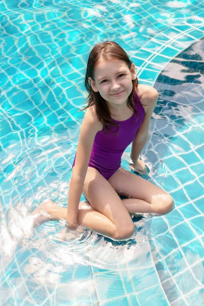 Yüzme havuzu kenarında oturan sevimli gülümseyen varoluş kız. Seyahat, tatil, çocukluk kavramı