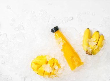 Düz manzaralı, buzlu muz ve mangolu sarı meyve suyu şişesi. Sağlıklı yaşam tarzı kavramı. Vegan, vejetaryen yemeği