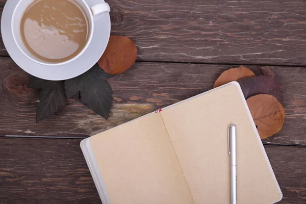 kahve ve sonbahar yaprakları ahşap arka planda defter ile