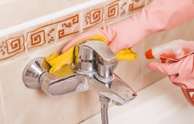 Lastik eldivenli kadın banyoyu paçavrayla temizliyor.