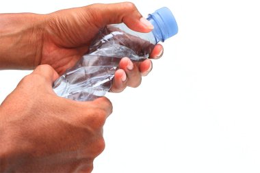 Beyaz arka planda plastik maden suyu şişesini sıkan eller.