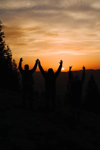 Morning sunrise in the mountains, silhouette of people who rejoice and stretch their hands to the sky
