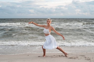 Genç güzel balerin dans ve deniz arka plan dışında poz.