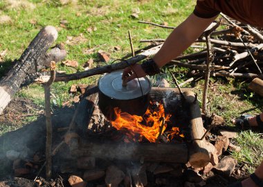 İnsan eli dağların arasında bir yeşil dağ çayır ateşe ısıtmalı bir eski küçük kazan yükseltir
