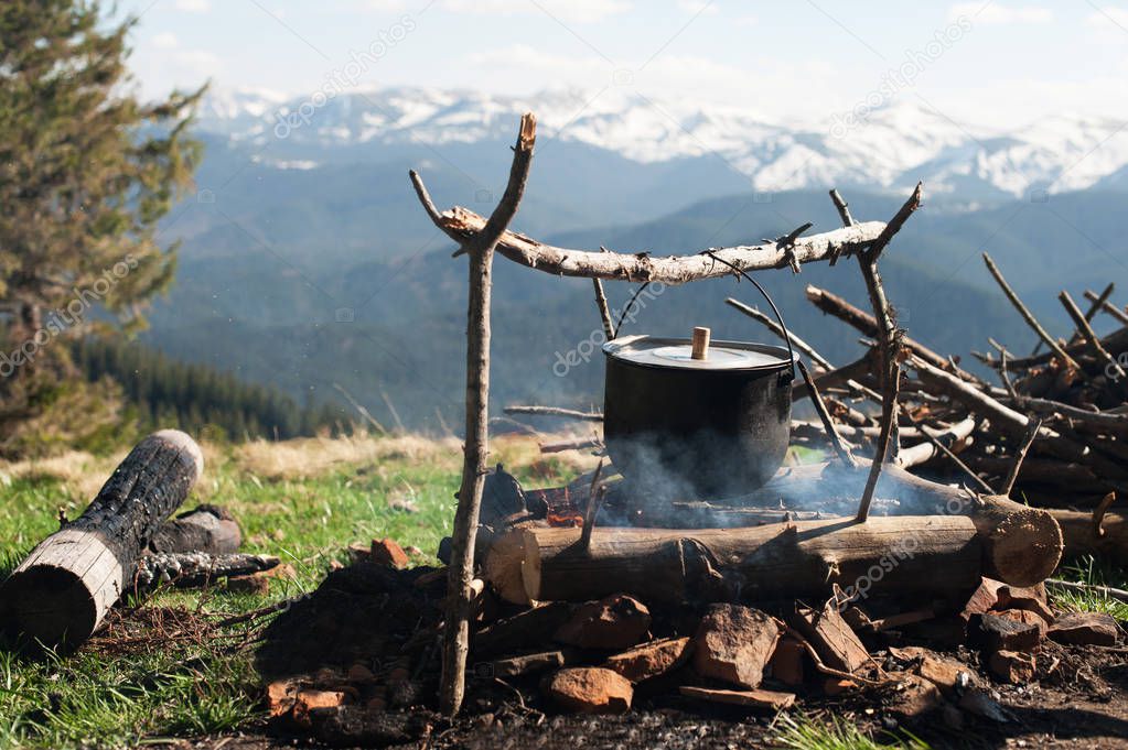 An old little boiler is heated on a fire on a green mountain meadow among the mountains