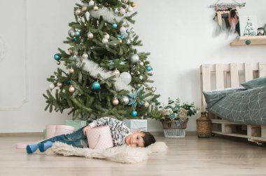 Hediye kutusu Noel ağacı Noel arifesinde evde yakınındaki küçük çocuk. Kış dekorasyonu ile hafif yatak odasında genç çocuk. Evde mutlu bir aile. Yılbaşı yeni yıl kutlama kavramı için Aralık zaman