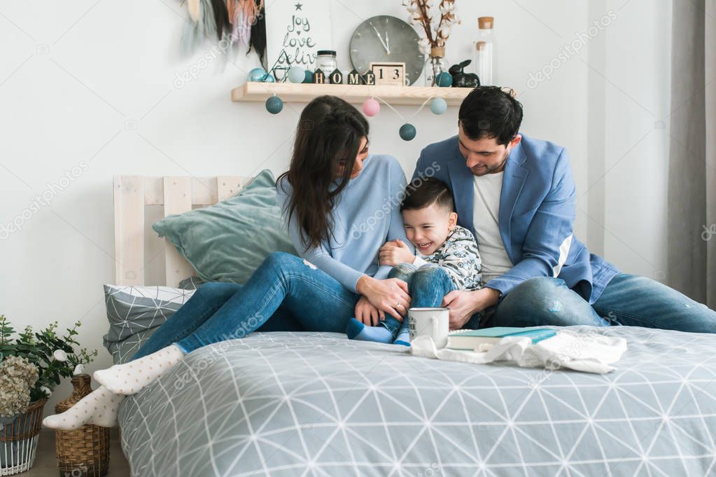 Young happy family of three laying on bed near christmas tree. Mother and father having fun with son in living room. Happy parenting concept. New Year's interior
