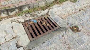 Top Down View of Rusted Storm Drain Grate with Debris and Street Cobblestones