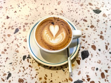 Terrazzo masasında beyaz bir fincanda servis edilen kahve yapraklı latte. 