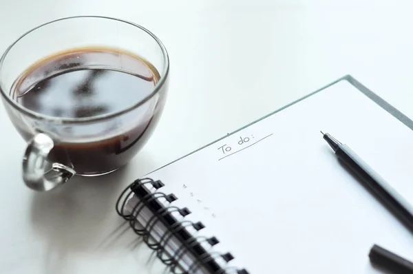Yapılacaklar listesi not defterinde. Yapılacaklar listesi yazmak. beyaz sayfa, siyah kalem, bir fincan kahve. Bir gün planlama. etkinlik planlama. el ile yazma.