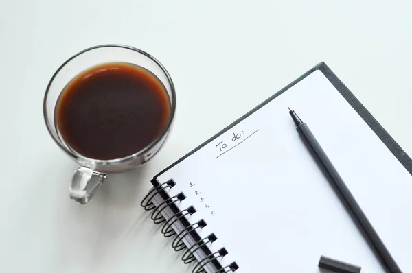 Yapılacaklar listesi not defterinde. Yapılacaklar listesi yazmak. beyaz sayfa, siyah kalem, bir fincan kahve. Bir gün planlama. etkinlik planlama. el ile yazma.