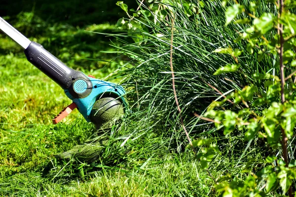 The simple moments of life, ordinary work in the garden -  man trimming grass with heavy-duty trimmer in the garden, suitable for trimming long lawn edges and larger hard-to-access areas