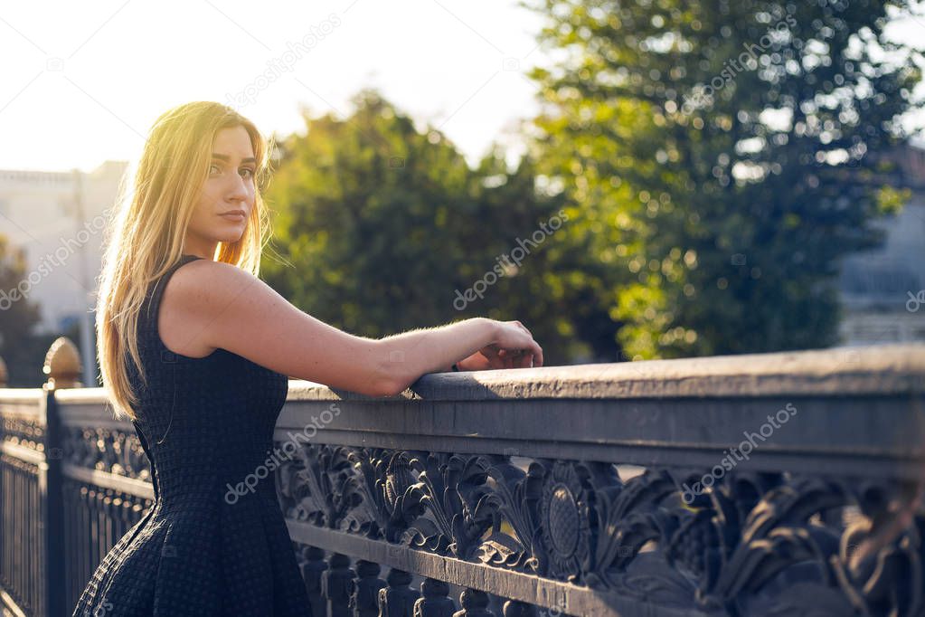 A young woman is near the old bridge fence. Old vintage town filled of the evening sun.