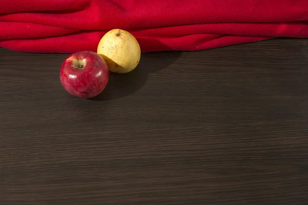 Red apple and yellow pear with red drapery on the wooden surface