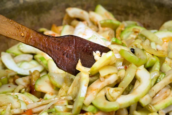 Zucchini salad cooking process. Wooden oiled spatula in.