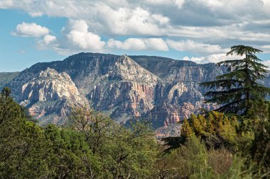 Sedona, Arizona, ABD 'de mavi gökyüzü altında geniş bir dağ silsilesi. Mavi gökyüzü altında tüylü beyaz bulutlar.