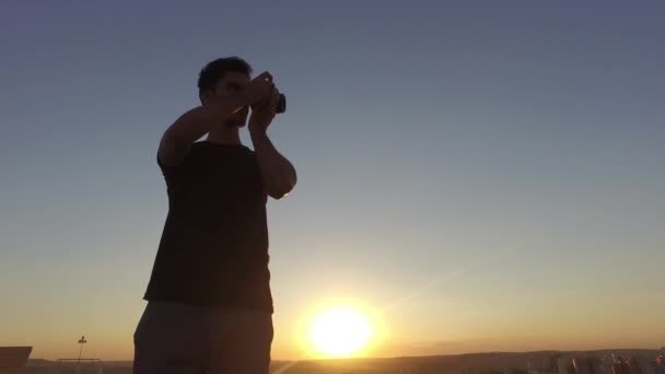 男摄影师在日落时在大楼顶上拍照 — 图库视频影像
