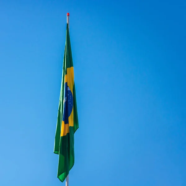 Braziliaanse vlag op paal zonder wind in de voorkant van de blauwe hemel. — Stockfoto