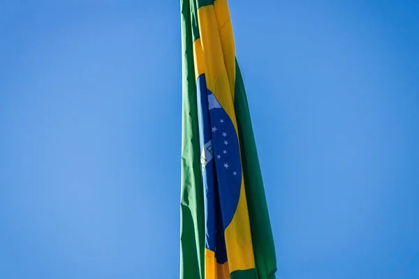 Bandeira brasileira no poste sem vento na frente do céu azul . — Fotografia de Stock